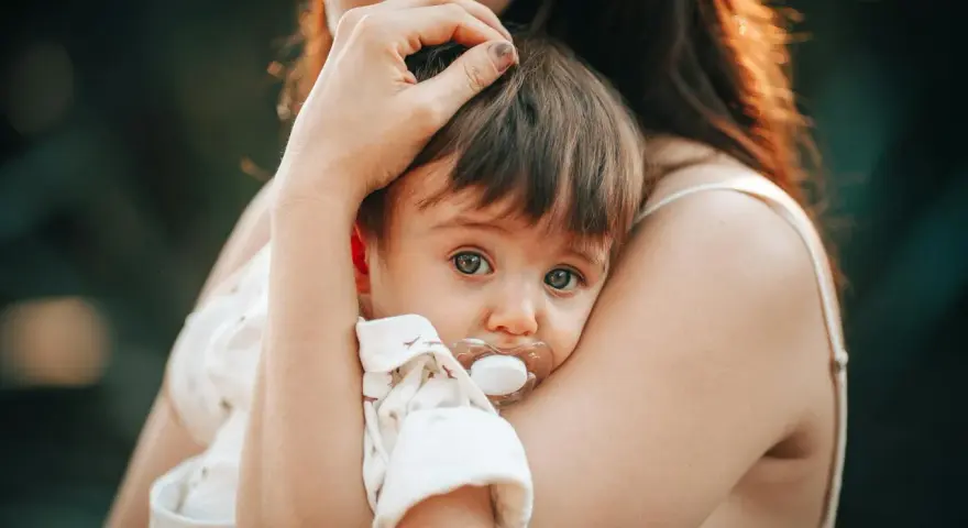 Bebé con chupete, acurrucado en brazos de su madre. Un momento tierno que nos hace pensar en cuando se inventó el chupete.
