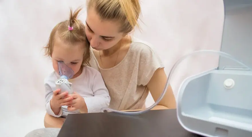 Madre consuela a su hija con bronquitis espástica mientras usa un nebulizador.