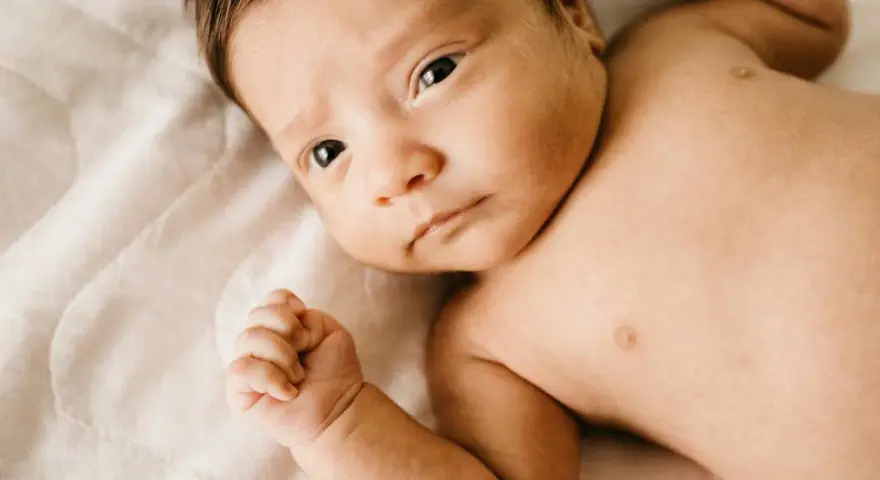 Bebé con mirada intensa, su puño cerrado y piel suave. Podría ser un signo de hipertonía en bebés, pero su expresión es serena.