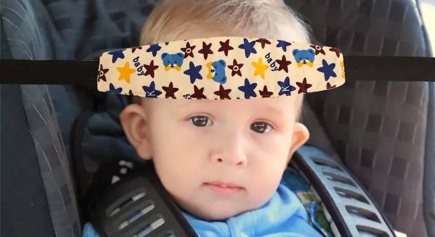 Un bebé con un arnés sujetacabezas con ositos y estrellas, esencial porque hay que sujetar la cabeza a los bebés en el coche.