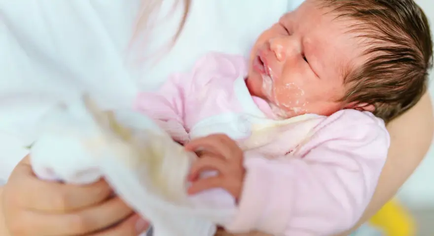 Bebé con leche regurgitada en la cara y ropa. El reflujo en bebés es normal, pero hay que saber cuándo preocuparse.