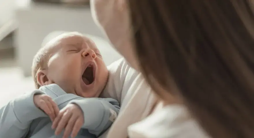 Bebé bosteza en brazos de su madre. Podría ser un signo de hipoglucemia bebé, pero también solo sueño.