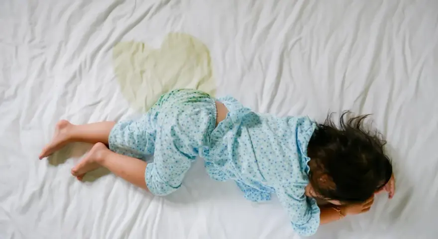 Niño en cama con mancha de orina. Buscando enuresis nocturna infantil remedios naturales para ayudarle.