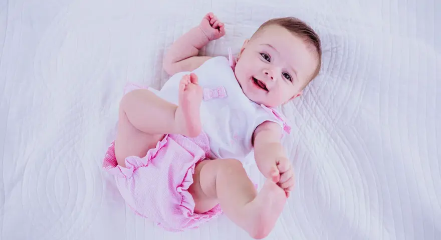 Bebé sonriente con un traje rosa y blanco, perfecto para inspirar nombres de niñas.