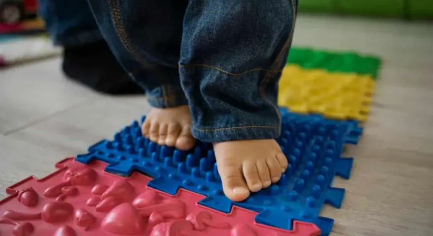 Pies descalzos de un niño sobre un tapete de rompecabezas texturizado, parte de juegos de coordinación para el desarrollo.