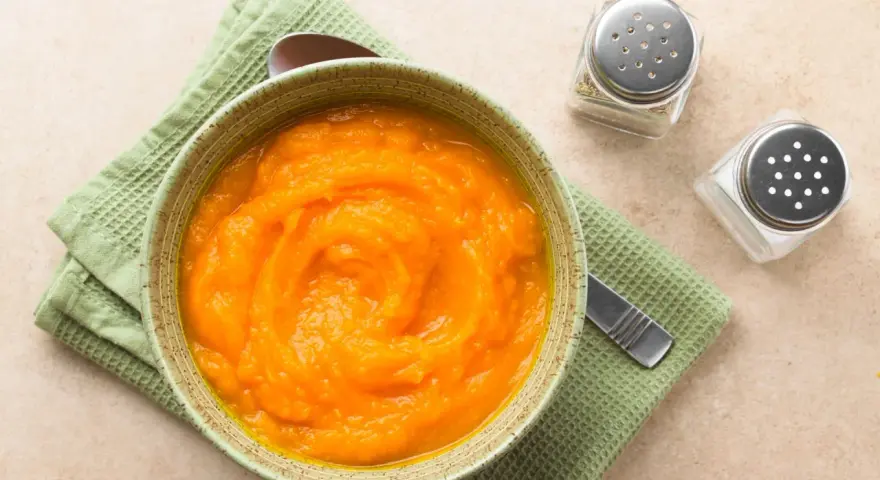 Puré de calabaza y patata para bebé, listo para congelar. Servido en un cuenco con una cuchara y saleros al lado.