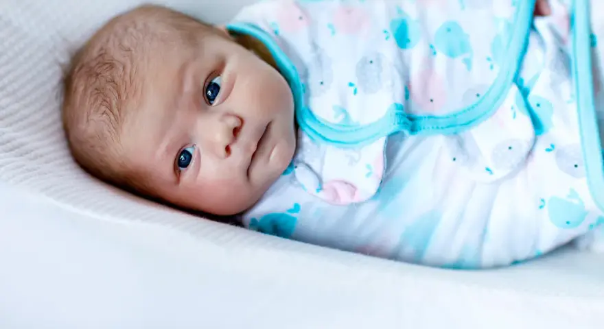 Un tierno bebé con ojos azules, envuelto en una mantita con ballenas, listo para arrullar.