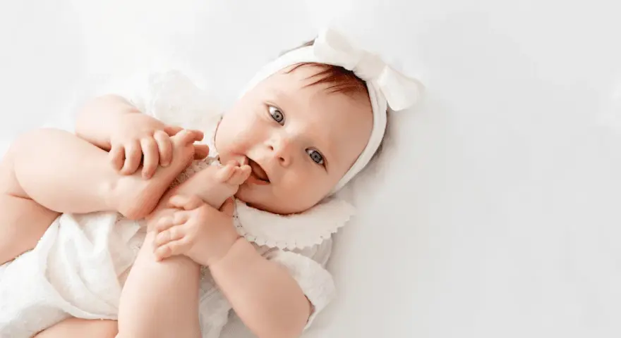 La bebé Cora, con su diadema de lazo blanco, juega con sus pies.