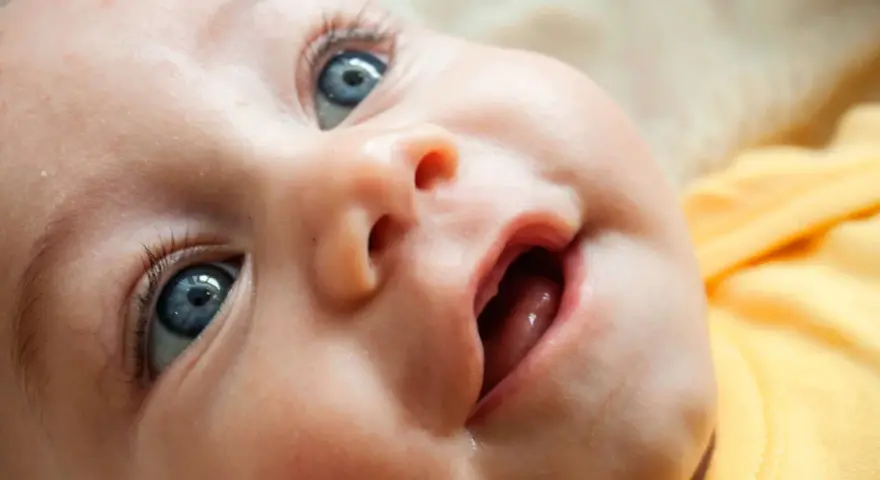 Bebé con ojos azules y boca abierta, mostrando las encías y los primeros dientes saliendo.