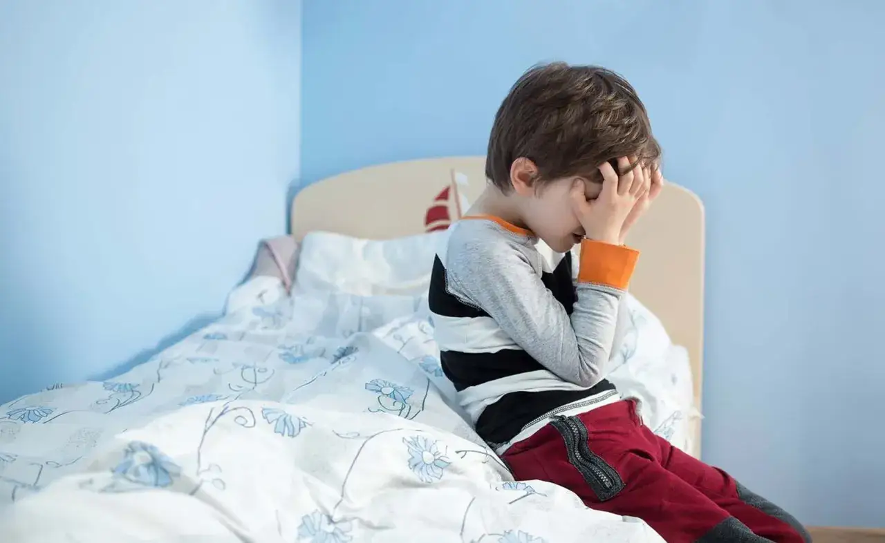 Ni&ntilde;o triste en la cama, preocupado por la enuresis nocturna infantil. Busca remedios naturales para superarla.