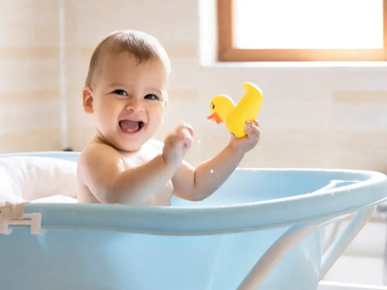 Un bebé sonriente juega con un patito de goma en la bañera. Es un buen momento para bañar a un bebé después de comer.