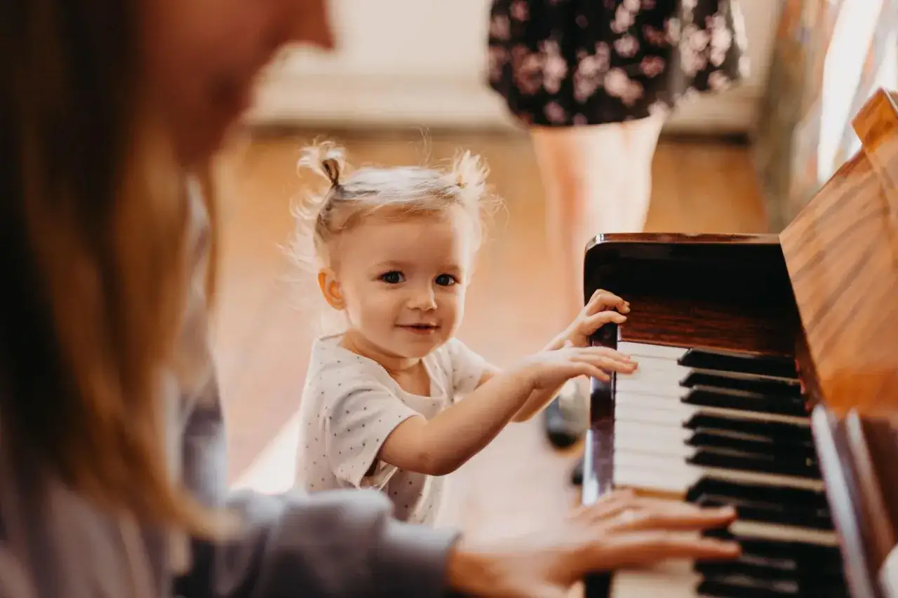 Niña rubia con dos coletas juega en un piano, disfrutando de la estimulación musical temprana.