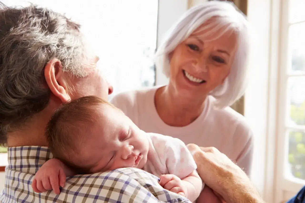 Un beb&eacute; duerme pl&aacute;cidamente en brazos de su abuelo, mientras su abuela sonr&iacute;e. Es un momento tierno cuando un beb&eacute; reconoce a sus abuelos.