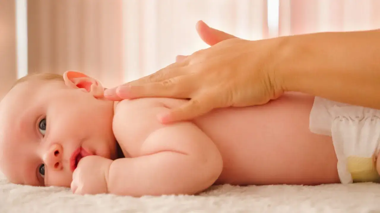 Una mano acaricia la espalda de un beb&eacute;, ofreciendo un reconfortante masaje infantil.