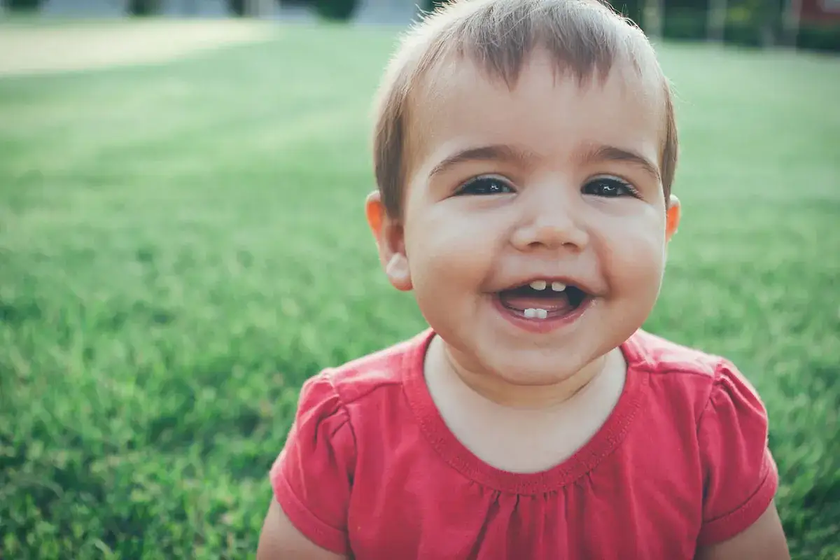Un beb&eacute; de 1 a&ntilde;o sin dientes r&iacute;e a carcajadas en el c&eacute;sped.