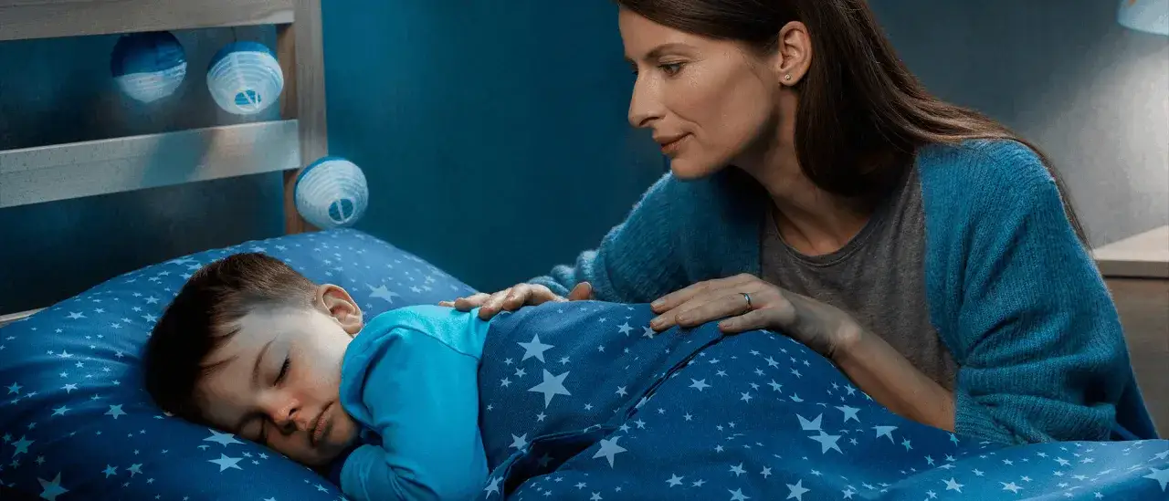 Madre consuela a su beb&eacute; que tiene muchos mocos y no puede dormir, acariciando su espalda mientras &eacute;l descansa en su cama estrellada.