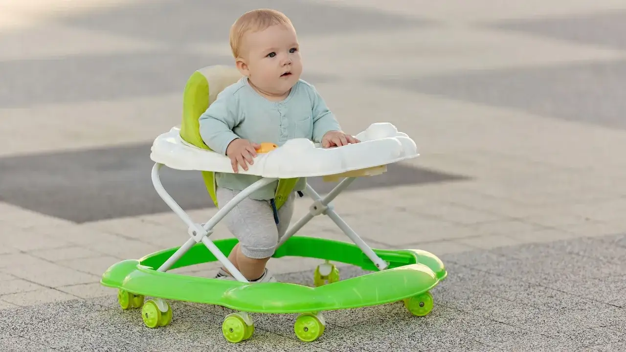 Un beb&eacute; rubio con ojos azules explora el mundo en su andador verde. &iexcl;Taka taka ni&ntilde;os, a caminar!