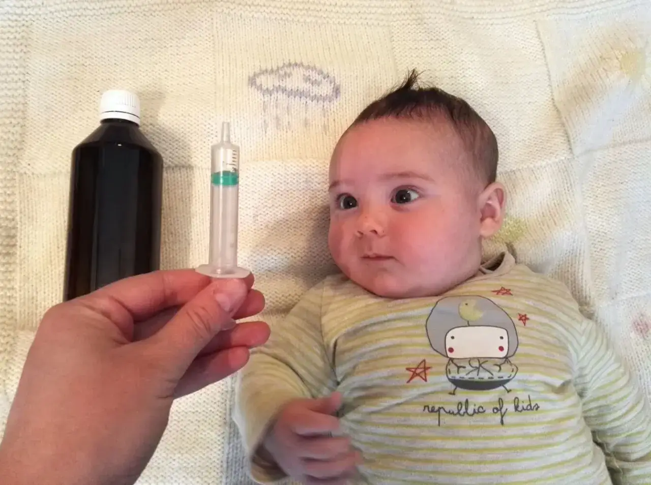 Beb&eacute; de 1 mes con resfriado, listo para su medicina. Una mano sostiene una jeringa con l&iacute;quido.