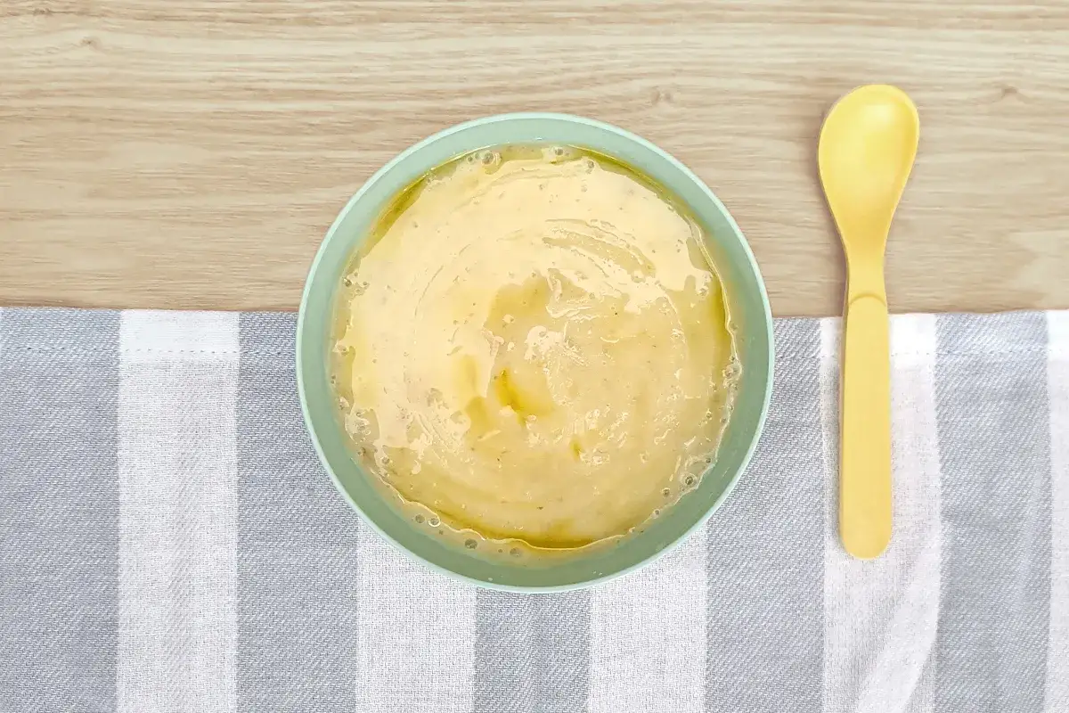 Pur&eacute; de patata para beb&eacute; listo para congelar. Un taz&oacute;n verde menta con pur&eacute; cremoso y una cuchara amarilla al lado.