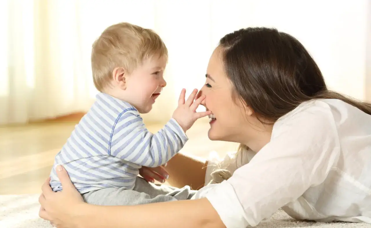 Un bebé con una camiseta a rayas toca la nariz de su madre, riendo. Es un momento tierno de cuando imitan los bebes.