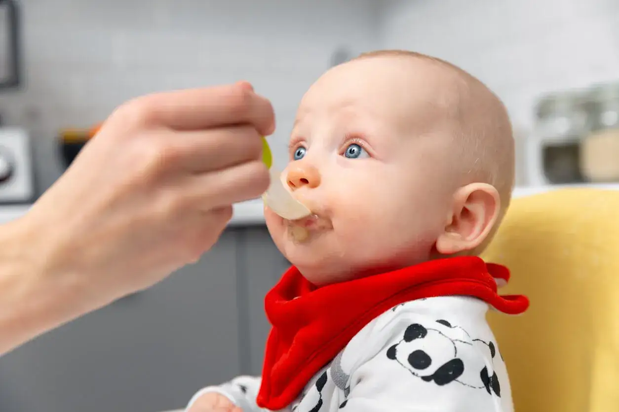 Beb&eacute; con ojos azules recibe pur&eacute; de legumbres bebes con una cuchara.