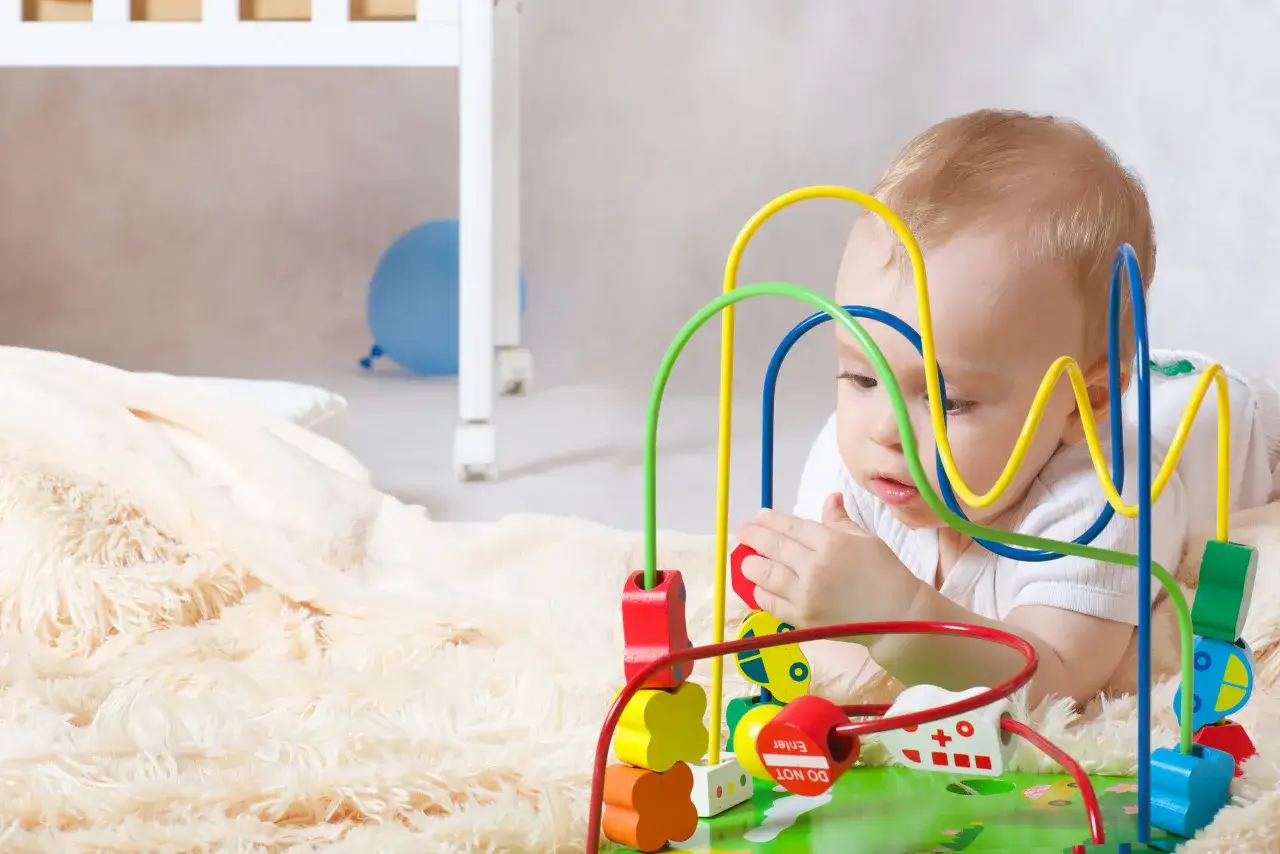 Un bebé de 9 meses juega concentrado con un juguete de cuentas de colores.