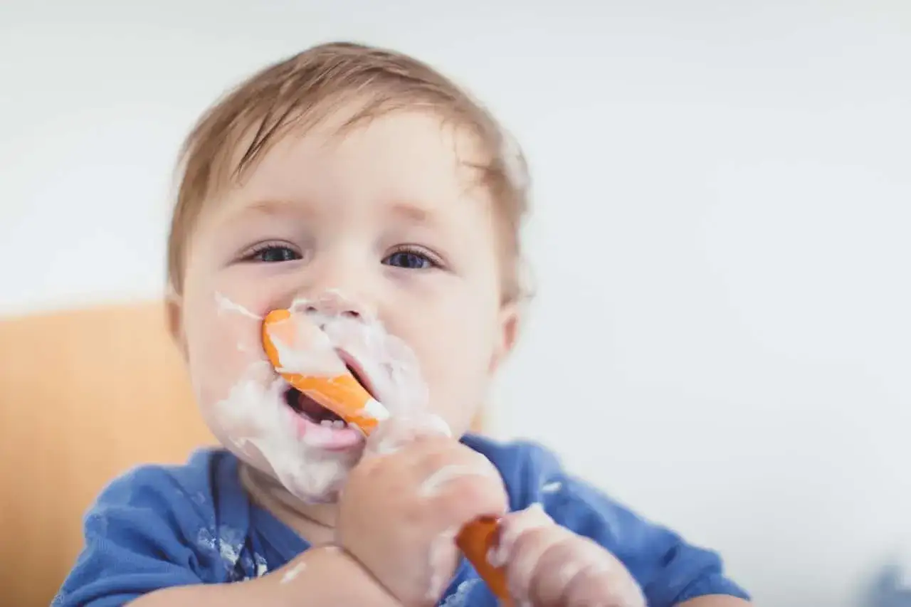 Beb&eacute; con cara y cuchara cubiertas de yogur, disfrutando de su comida. &iexcl;Momento perfecto cuando puedo dar yogur a mi beb&eacute;!