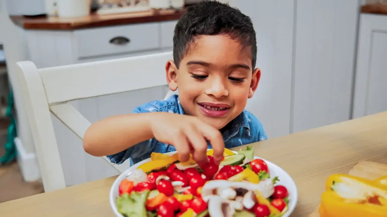 Ni&ntilde;o sonriente elige tomates de una ensalada colorida, un paso clave para subir defensas ni&ntilde;os.