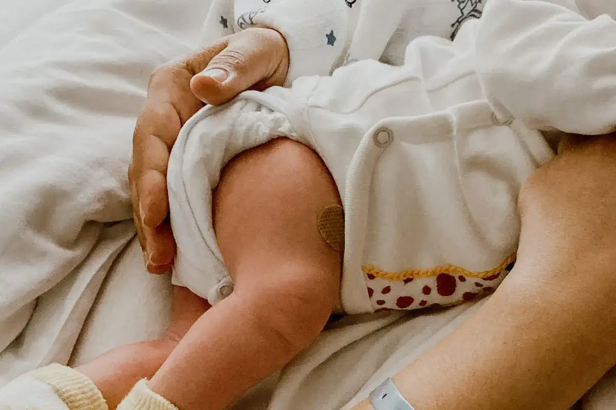 Pierna de bebé con parche, quizás en tratamiento para la hipertonía en bebés. Una mano adulta lo sostiene con ternura.