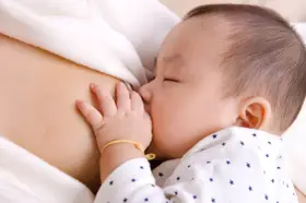 Bebé asiático durmiendo mientras se alimenta, mostrando el reflejo de succión. Su mano pequeña descansa sobre el pecho de su madre.