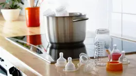 Preparación para desinfectar biberones con agua hirviendo. Tetinas y un biberón medidor listos en la encimera.