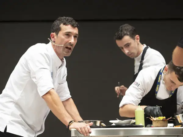 Eneko, chef con micrófono, dirige a su equipo en una demostración culinaria.