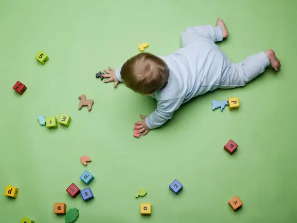 Bebé gateando entre bloques con letras y números, jugando con figuras de animales. Quizás buscando inspiración para nombres de niños originales.