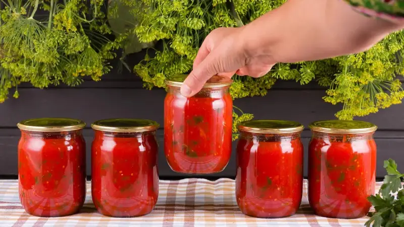 Mano toma un bote de cristal con tomate. Prepara para esterilizar botes cristal microondas.