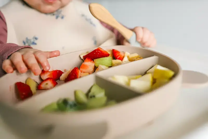 Bebé explorando fresas, kiwi y plátano en su plato. Es un buen momento para ofrecer fruta a los bebés.